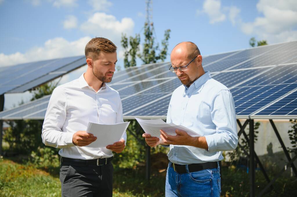 2人のエンジニアと太陽光発電所(太陽光パネル)は、システムの動作を確認するために歩く、世界のエネルギーを節約するための代替エネルギー、クリーンエネルギー生産のための太陽電池モジュールのアイデア. - 写真・画像