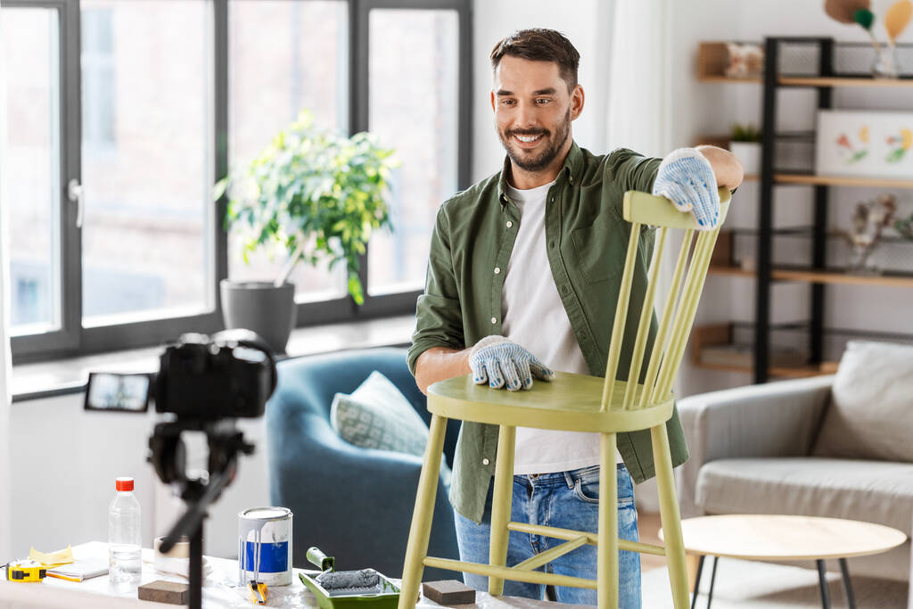 blogging, furniture restoration and home improvement concept - happy smiling man or blogger with camera showing old wooden chair renovation and recording tutorial video - Foto, Bild