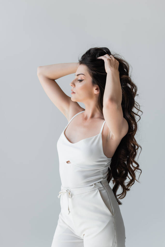 Side view of stylish brunette model touching long hair isolated on grey  - Fotó, kép