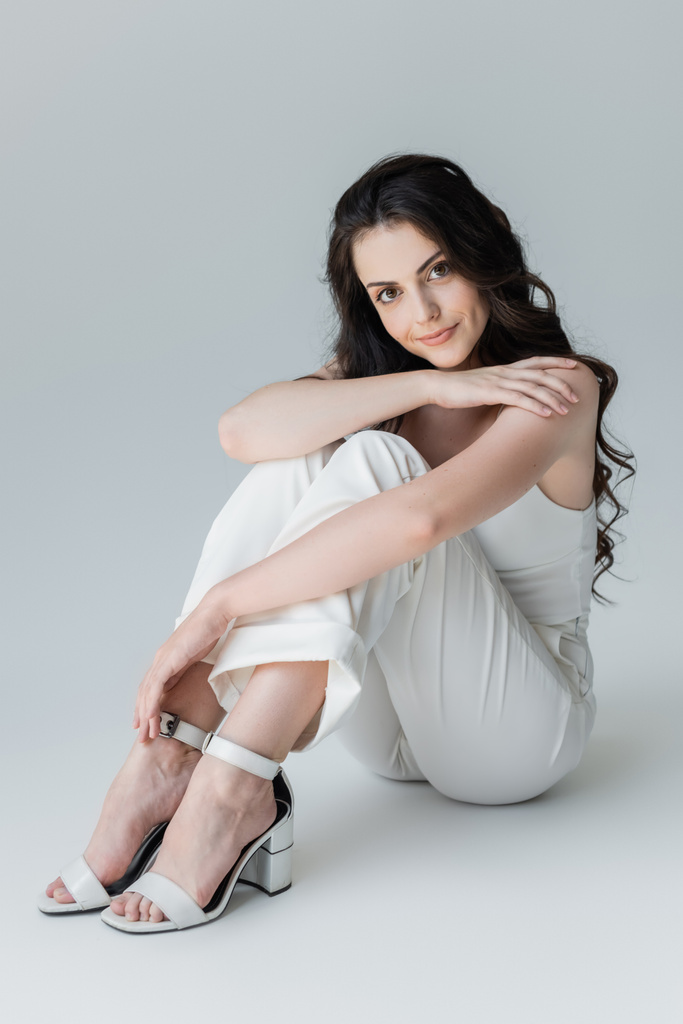 Full length of stylish model in heels and while clothes looking at camera on grey background - Zdjęcie, obraz