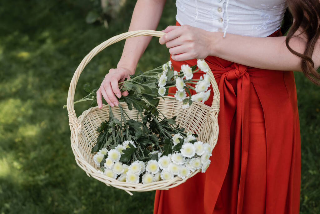Cropped view of stylish woman taking flowers from basket in park  - Zdjęcie, obraz