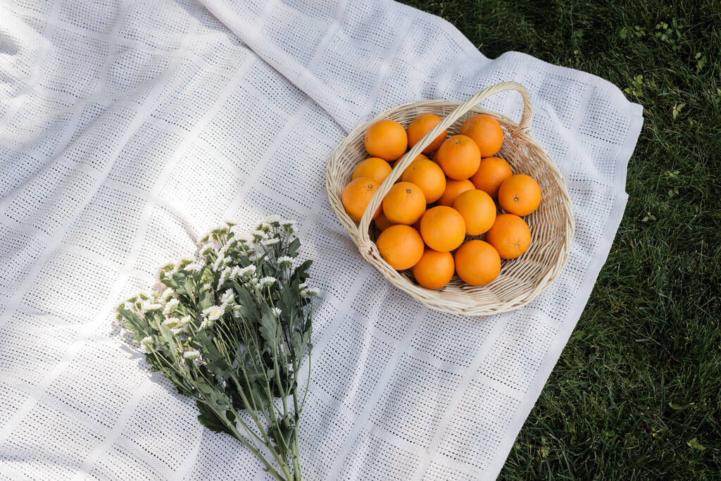 Top view of chamomiles and oranges in basket on blanket in park  - 写真・画像