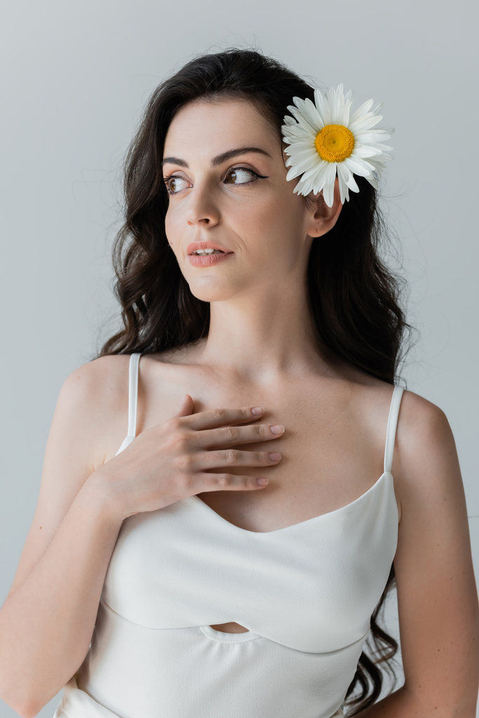 Pretty woman in white top and chamomile in hair looking away isolated on grey  - Foto, Bild