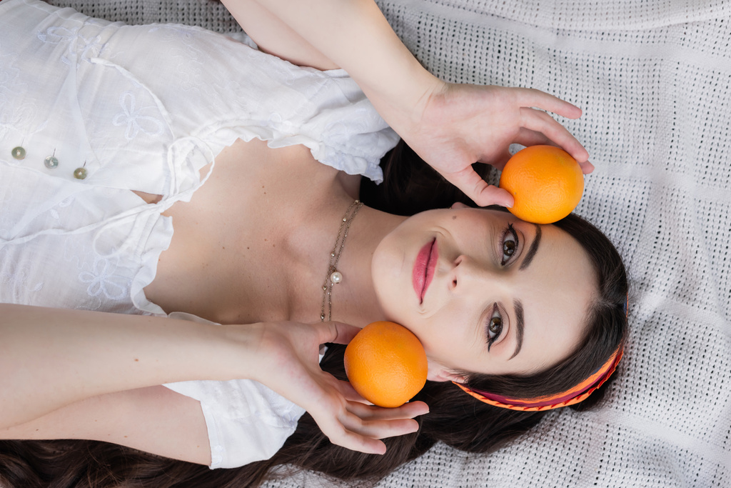 Top view of positive woman in blouse holding oranges on blanket in park  - Fotoğraf, Görsel