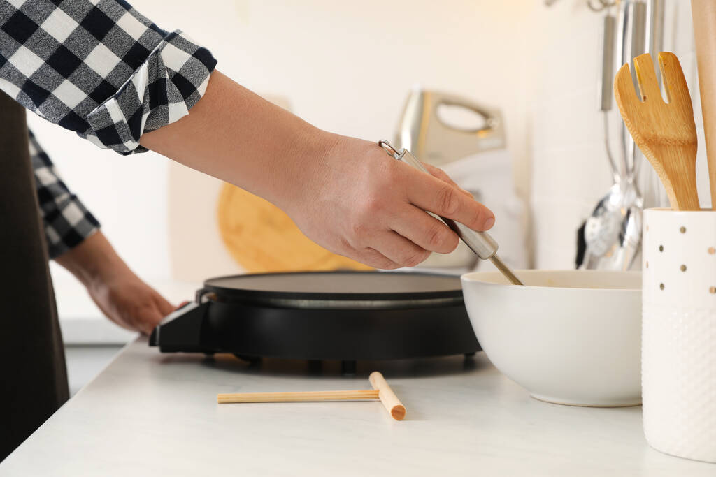 Man cooking delicious crepe on electric pancake maker in kitchen, closeup - Foto, Bild