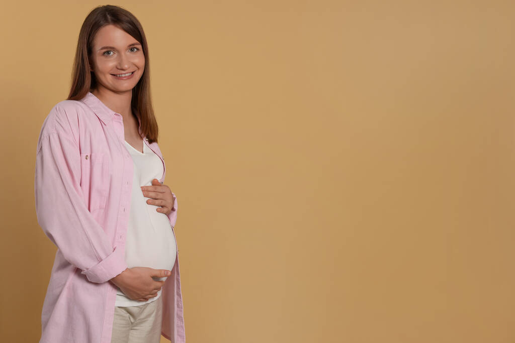 Ευτυχισμένη νεαρή έγκυος γυναίκα σε ανοιχτό καφέ φόντο. Χώρος για κείμενο - Φωτογραφία, εικόνα