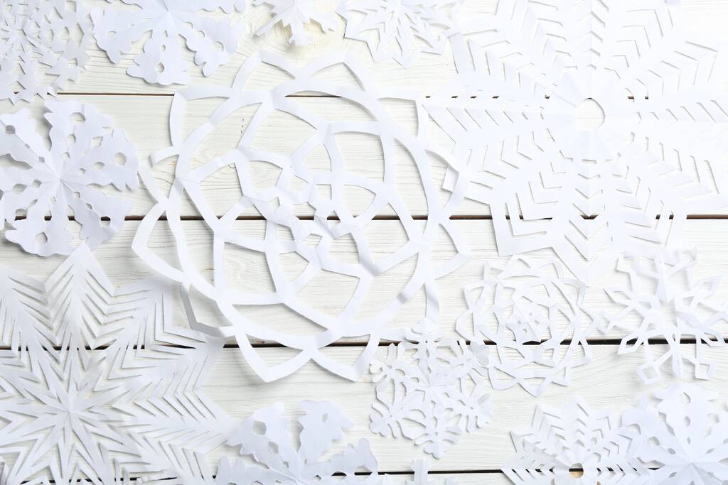 Πολλές νιφάδες χιονιού χαρτί σε λευκό ξύλινο φόντο, επίπεδη lay - Φωτογραφία, εικόνα
