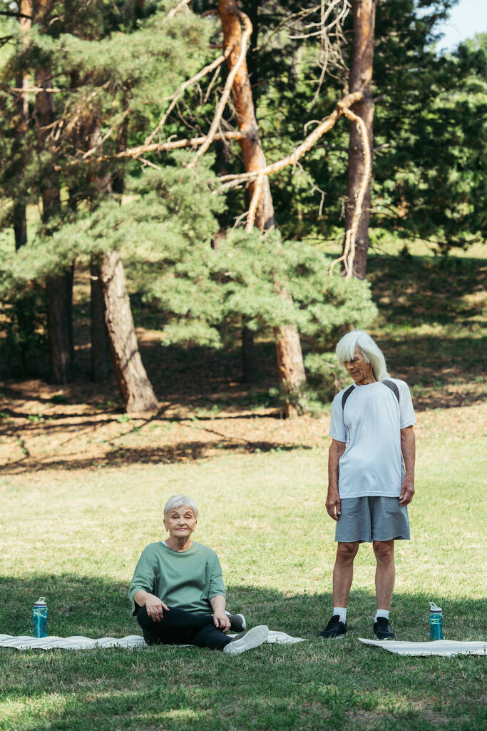 senior woman sitting on fitness mat near husband with grey hair in park - Valokuva, kuva