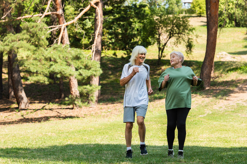 full length of senior couple in sportswear running in green park  - Photo, Image
