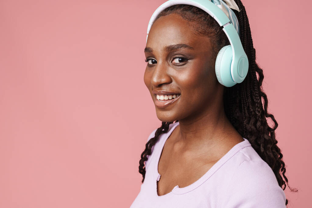 Black young woman smiling while listening music with headphones isolated over pink wall - Zdjęcie, obraz