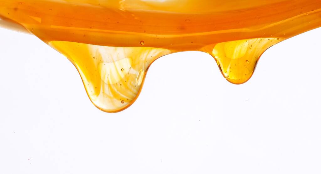 A closeup of honey dripping on a white background - Photo, Image