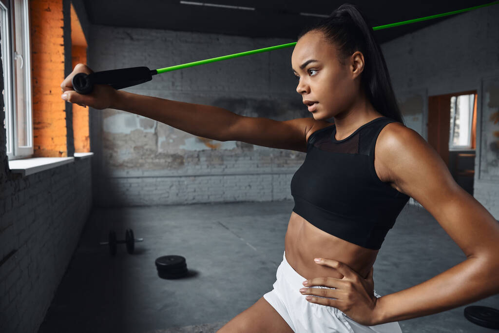 Confident young woman exercising with elastic resistance band in gym - Foto, Imagem