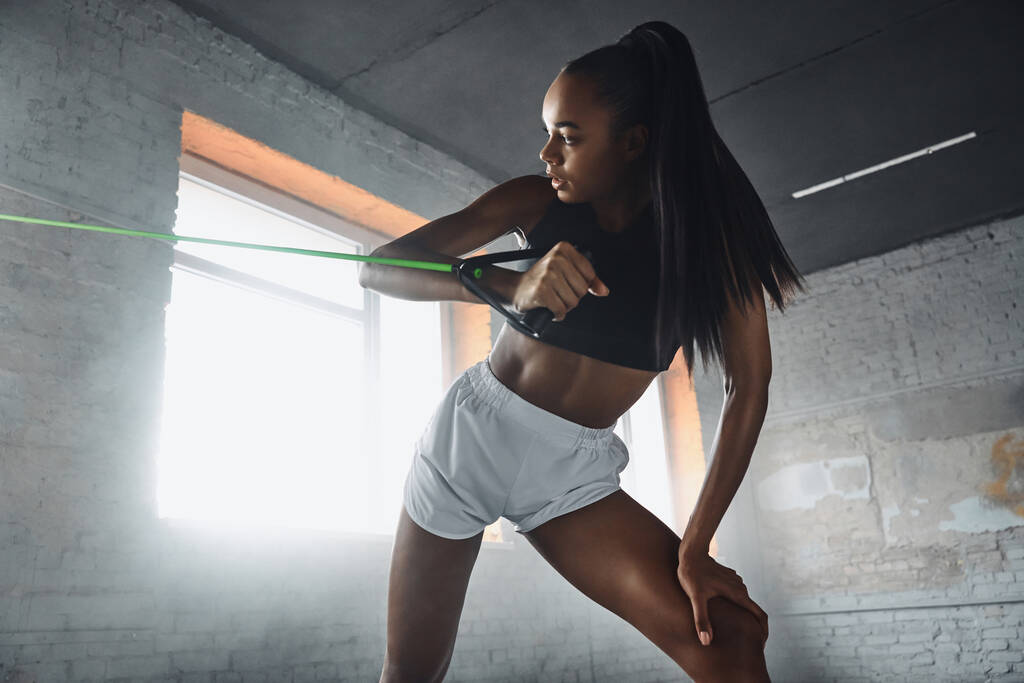 Confident young African woman exercising with elastic resistance band in gym - Valokuva, kuva