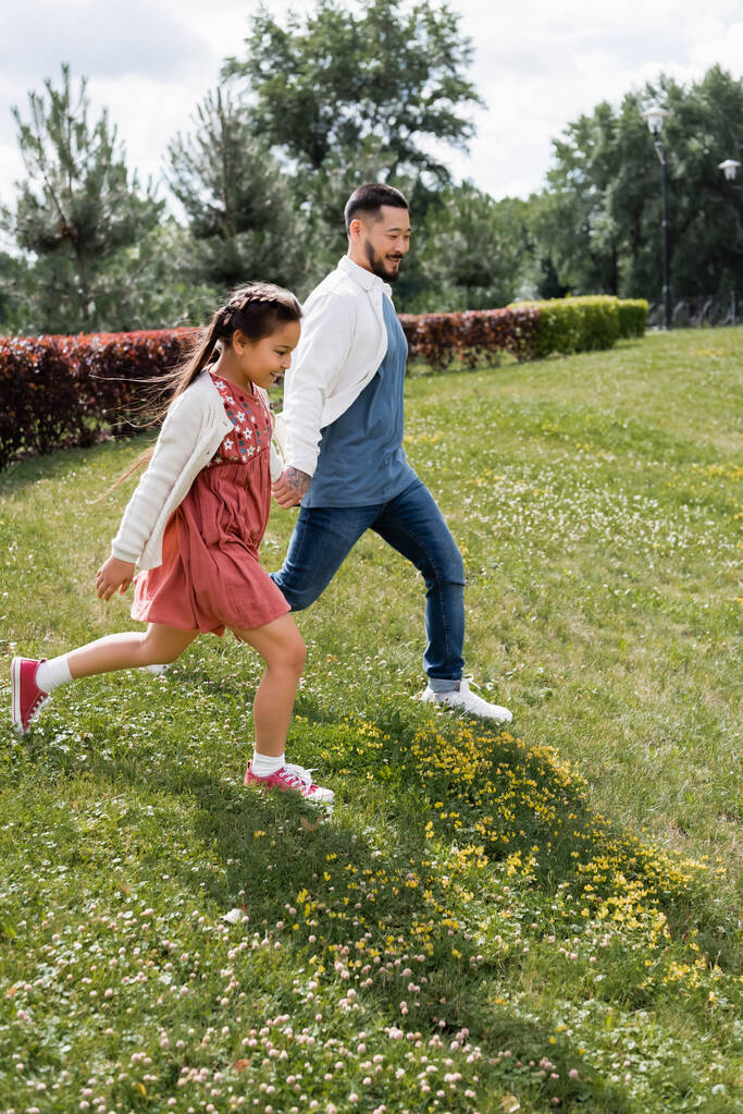 Asian girl holding hand of dad while running in park  - Photo, image