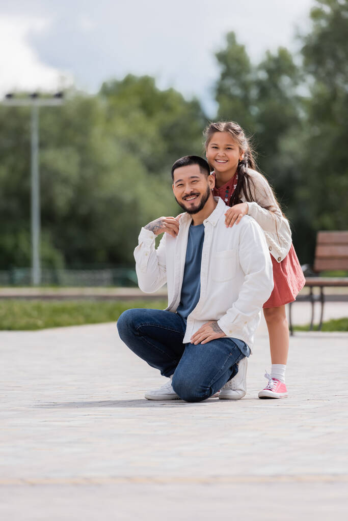 Smiling asian child hugging tattooed father in park  - Foto, Imagem