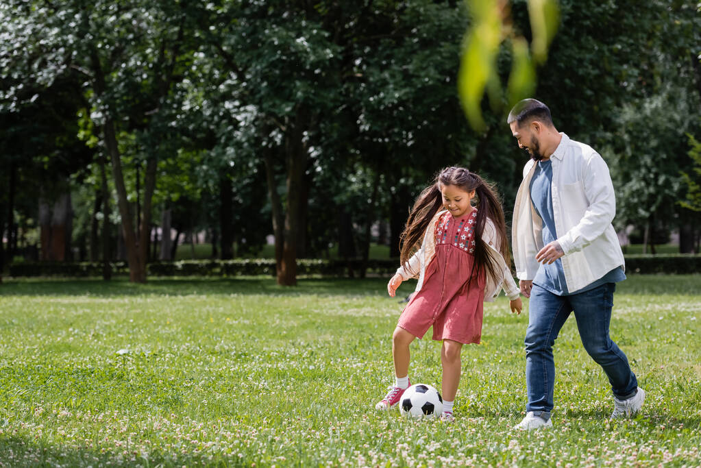 Cheerful asian kid playing football with dad on meadow in park  - Foto, Imagem