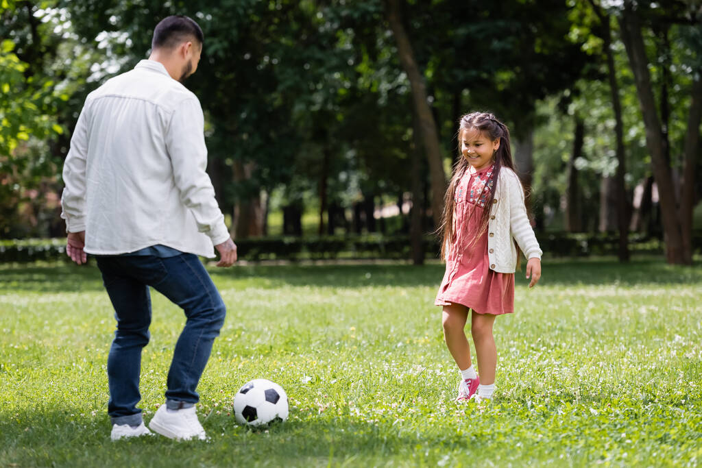 Χαμογελώντας ασιατικό παιδί παίζει ποδόσφαιρο με τον πατέρα στο πάρκο το καλοκαίρι  - Φωτογραφία, εικόνα