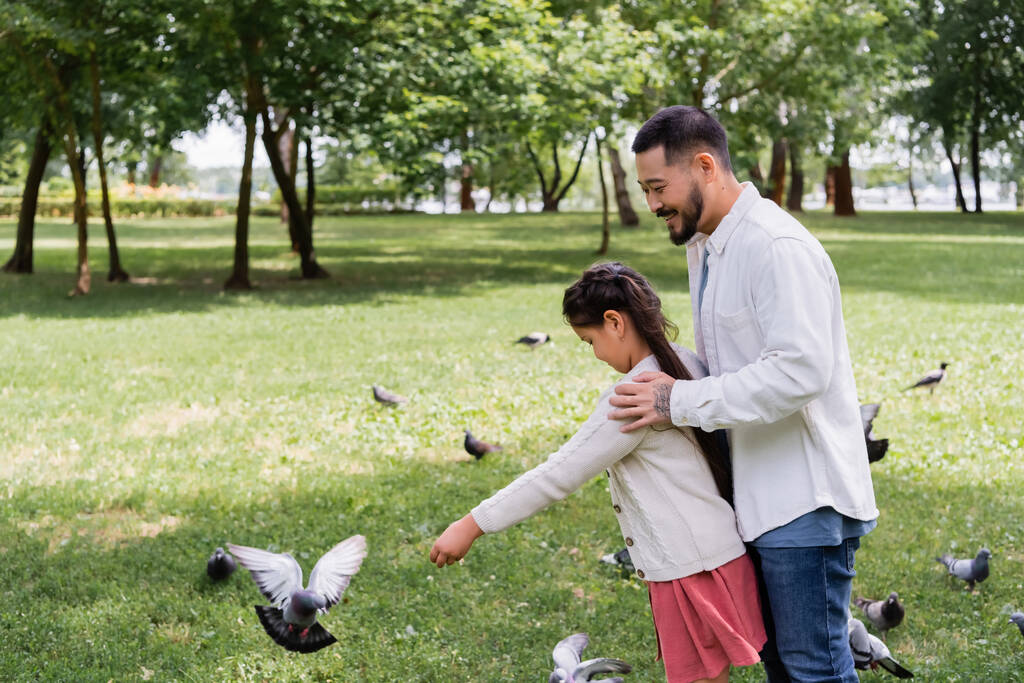 Тато з Азії обіймає доньку біля пташок у літньому парку.  - Фото, зображення