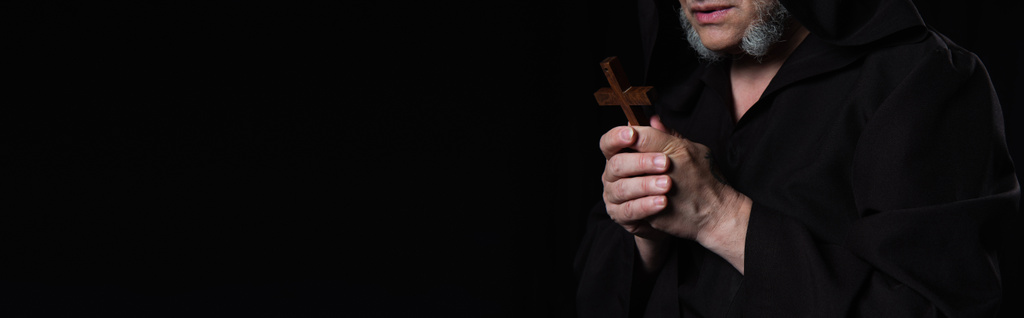 gedeeltelijk zicht op monnik met heilig kruisbeeld biddend geïsoleerd op zwart, banier - Foto, afbeelding