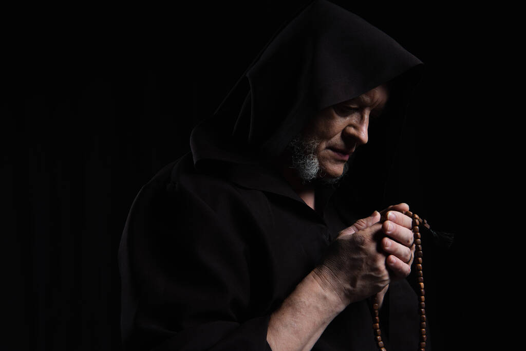 フード付きのローブに身を包んだ謎の司祭ブラックに孤立したバラ色のビーズで祈る - 写真・画像