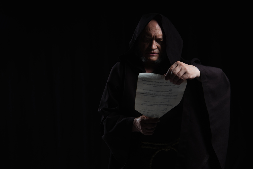 moine en soutane à capuchon lisant manuscrit médiéval isolé sur noir - Photo, image