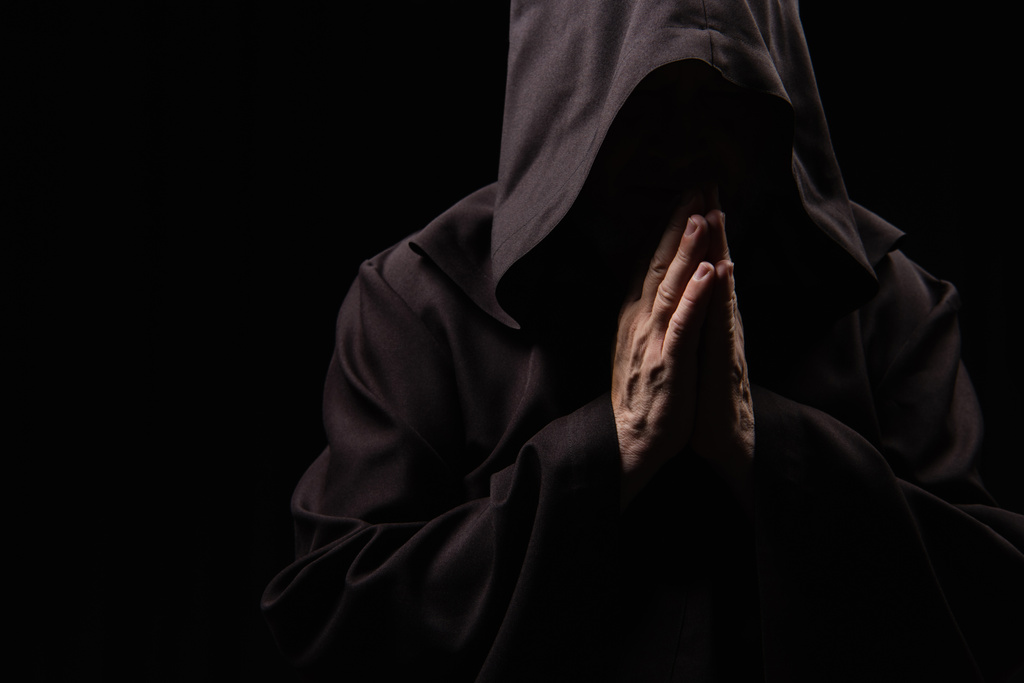 monje medieval anónimo en capilla rezando aislado en negro - Foto, Imagen