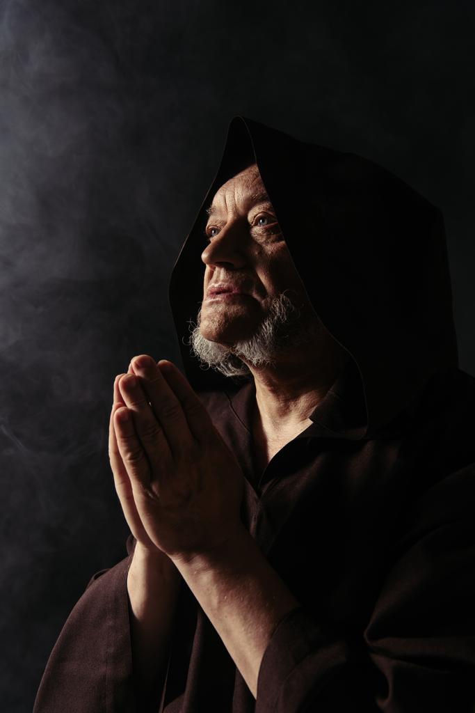 hogepriester met biddende handen wegkijkend op zwarte achtergrond - Foto, afbeelding