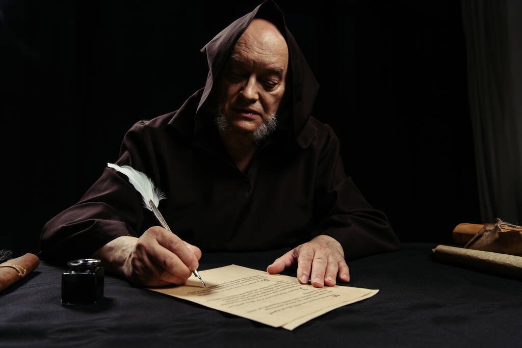 ksiądz w kapturze pisze kronikę na pergaminie odizolowanym na czarno - Zdjęcie, obraz