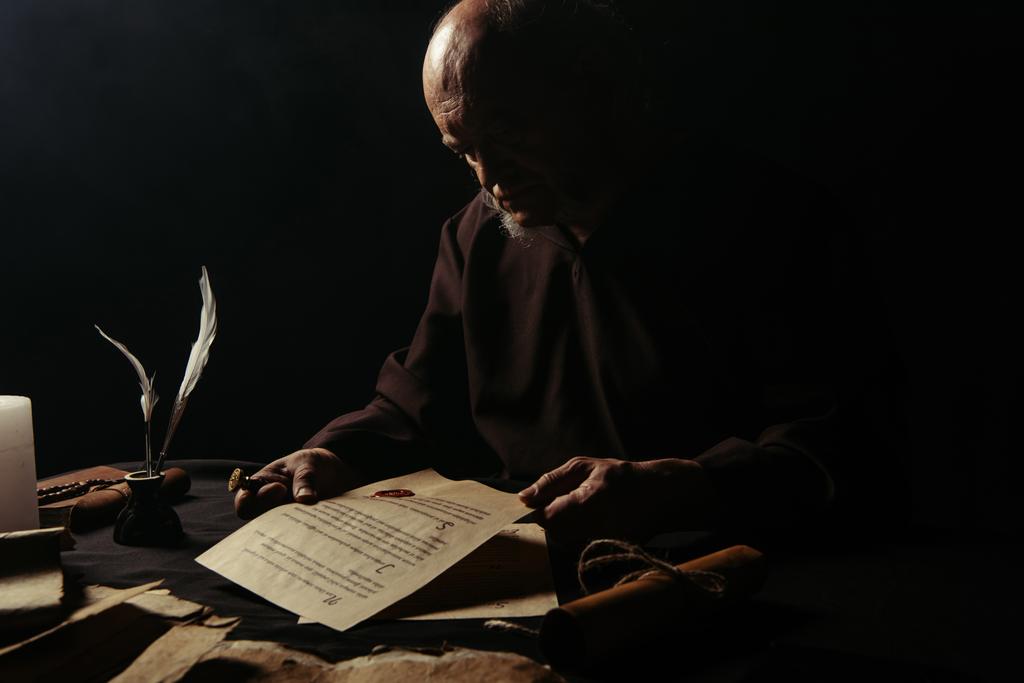 Kıdemli keşiş, siyah üzerine balmumu mühür yapıştırılmış el yazmasına bakıyor. - Fotoğraf, Görsel