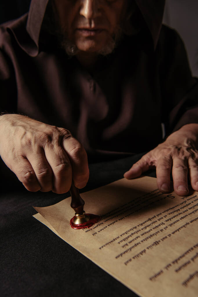 cropped view of priest putting wax seal on ancient chronicle isolated on black - Photo, Image