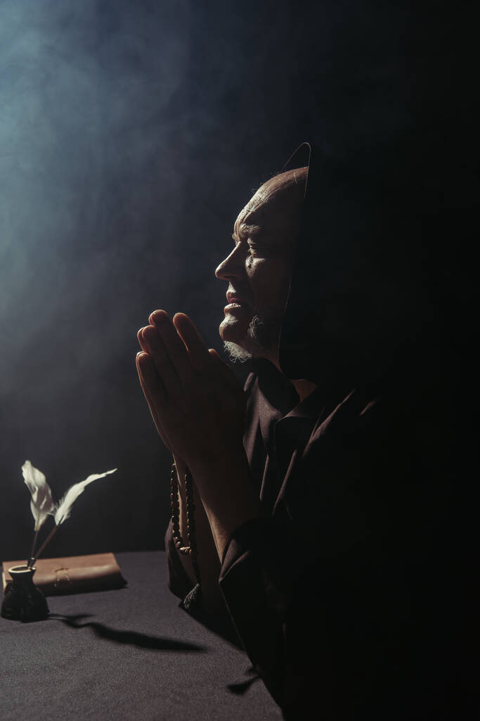 старший священик з розарійним бісером молиться біля чорнильного горщика з квітами на чорному з димом
 - Фото, зображення