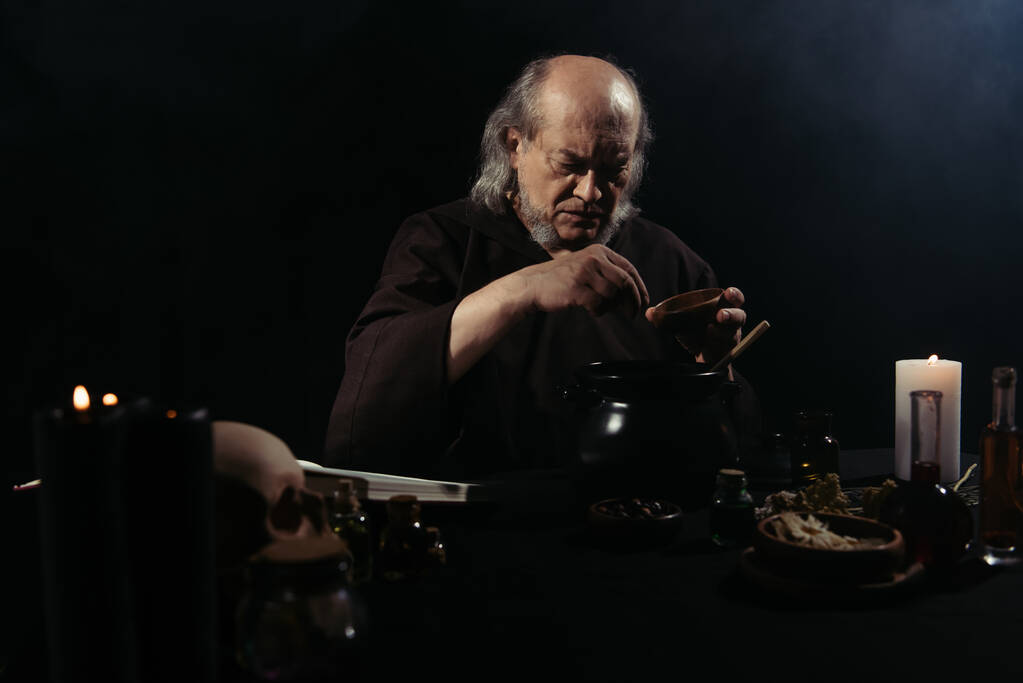 middeleeuwse alchemist bereidt toverdrank 's nachts geïsoleerd op zwart - Foto, afbeelding