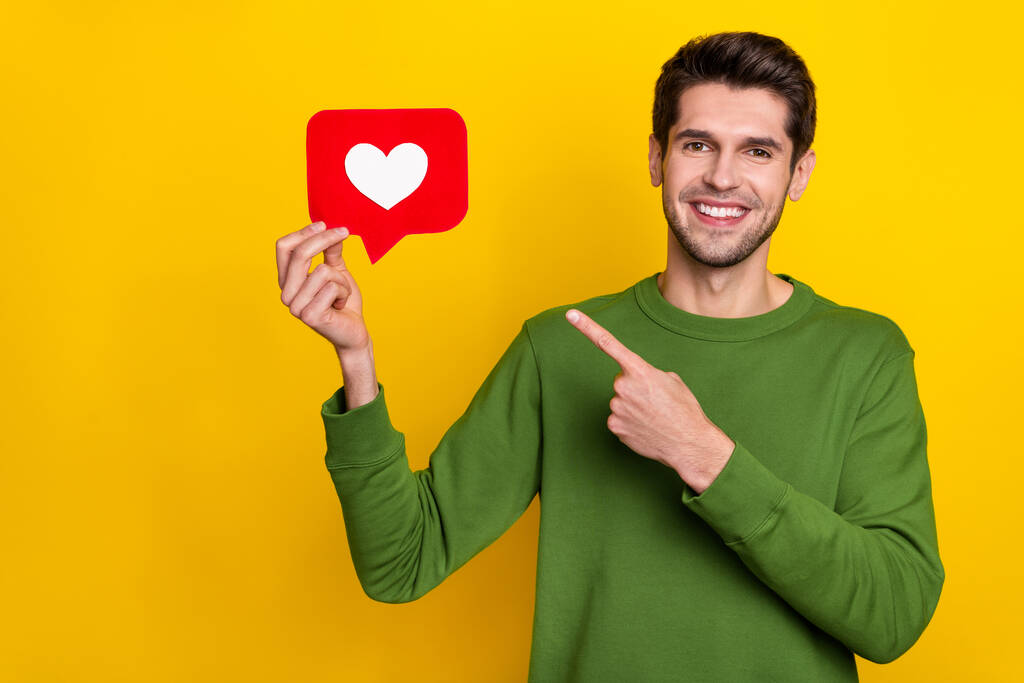 Photo of pretty cute young guy wear green sweater pointing finger heart like sign isolated yellow color background. - Fotografie, Obrázek