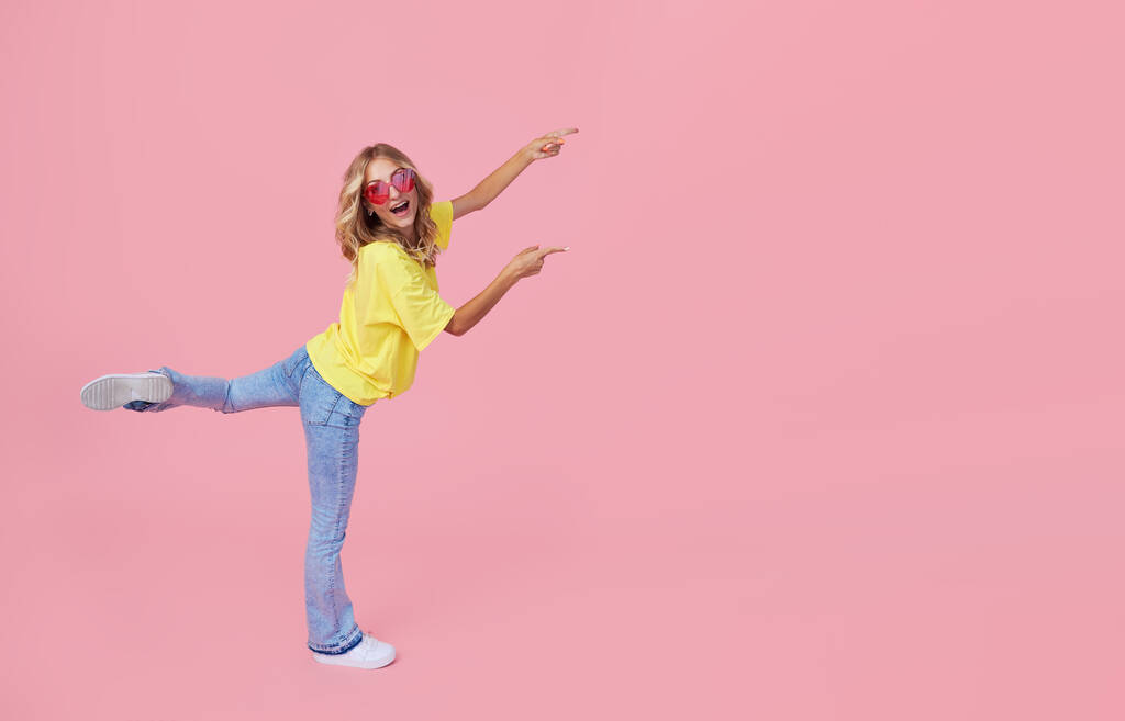 Pełen portret radosnej młodej kobiety w luźnych ubraniach skaczącej i świętującej na różowym tle - Zdjęcie, obraz