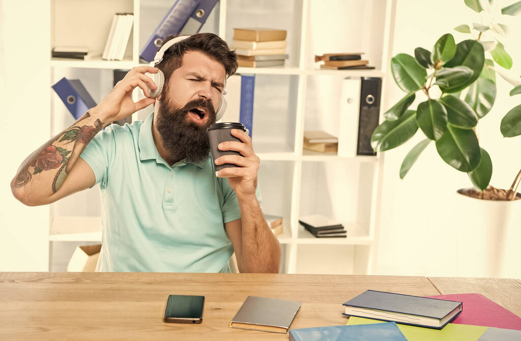 Happy man singing to takeaway cup listening to song in headphones in office, music. - Foto, Imagem