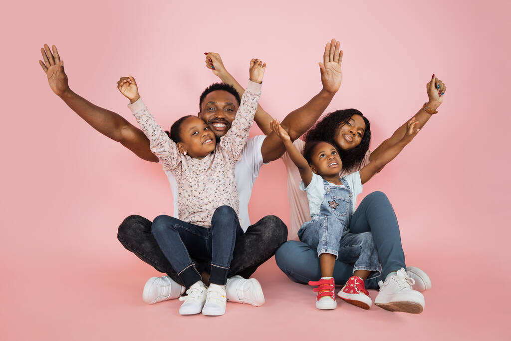 Family fun. Young african american parents spending time with their little daughters with open arms, laughing together over pink background, banner, panorama, copy space. - Zdjęcie, obraz