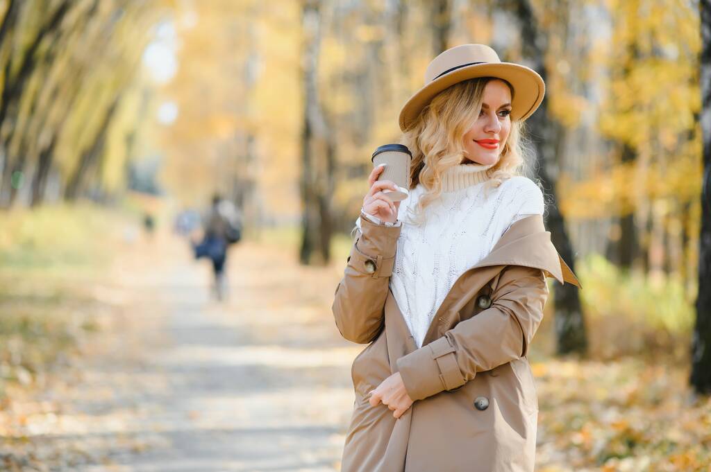 Όμορφη νεαρή γυναίκα με φλιτζάνι καφέ στο πάρκο φθινόπωρο. - Φωτογραφία, εικόνα