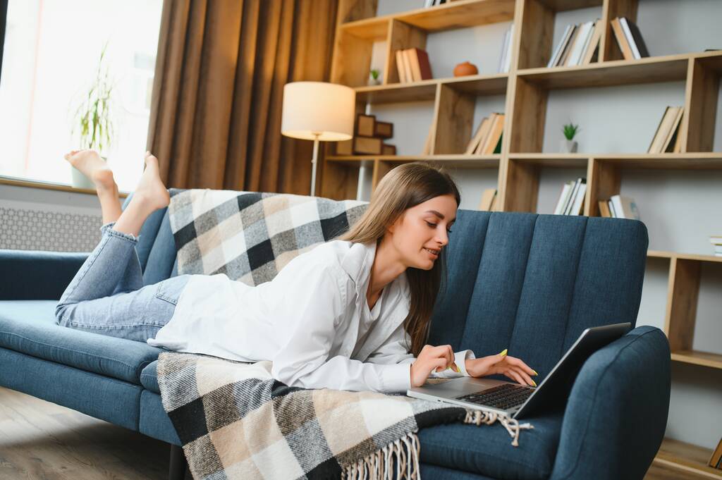 Mujer joven acostada en el sofá con el ordenador portátil
 - Foto, Imagen