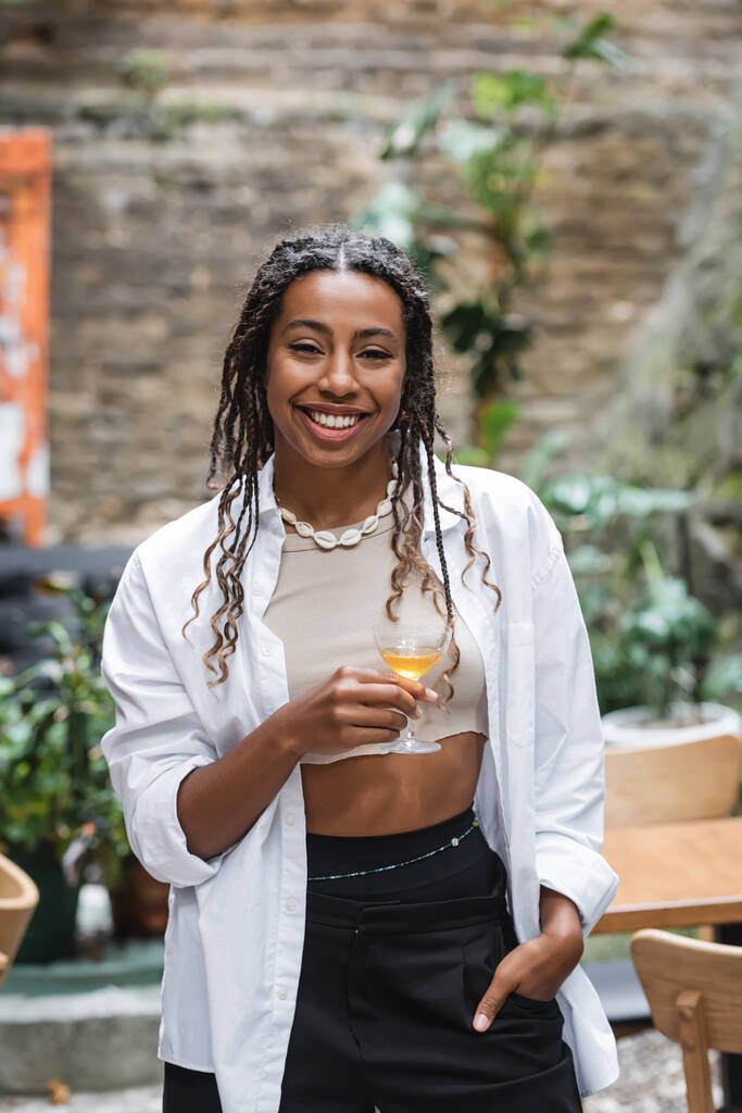 Позитивна афріканська жінка тримає склянку коктейлю на терасі кафе.  - Фото, зображення