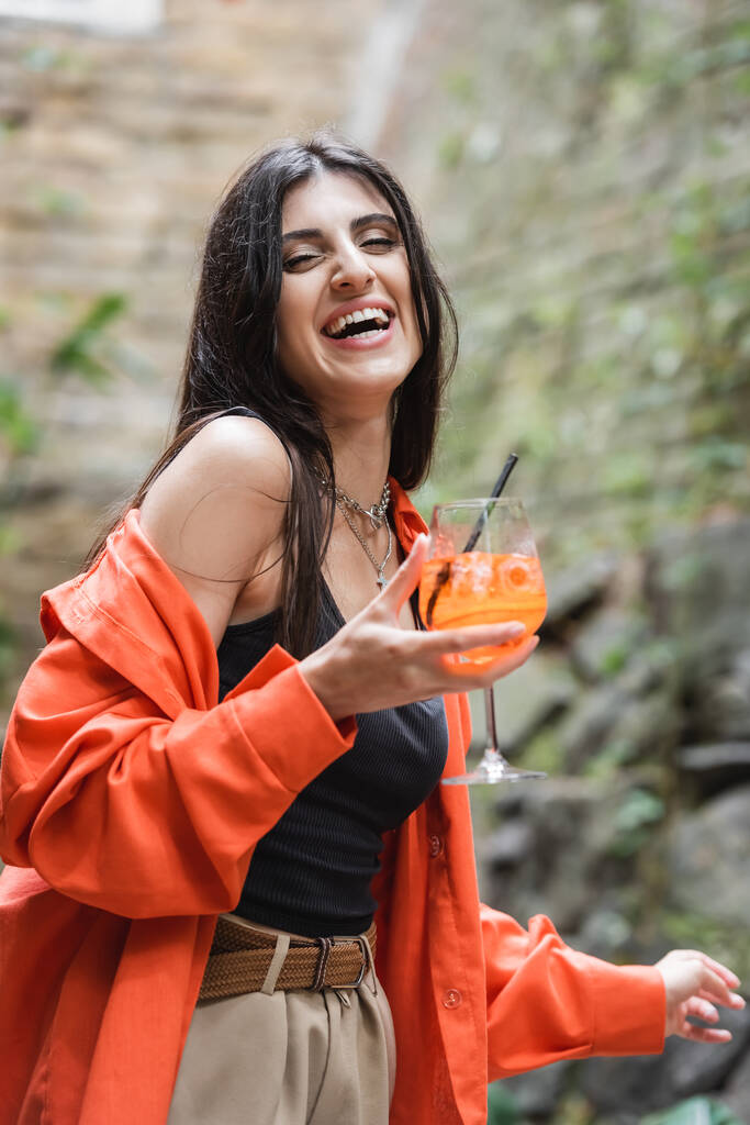 Positive woman holding glass of cocktail on terrace of cafe  - Fotó, kép