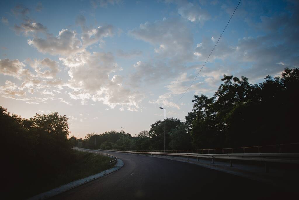 A vista de uma estrada rural vazia cercada por vegetação verde ao pôr do sol. - Foto, Imagem