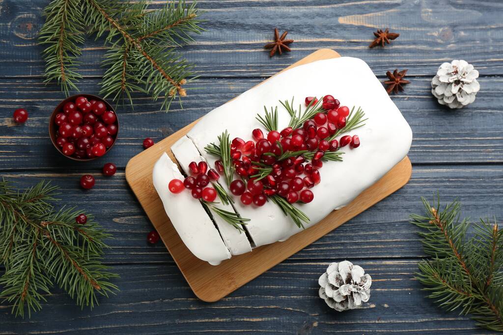 Пласка композиція з традиційним класичним різдвяним тортом з журавлиною, насінням гранату та розмарином на синьому дерев'яному столі
 - Фото, зображення