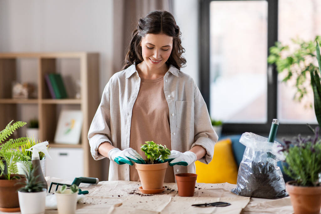 persone, giardinaggio e concetto di lavori domestici donna felice in guanti piantare fiori in vaso a casa - Foto, immagini