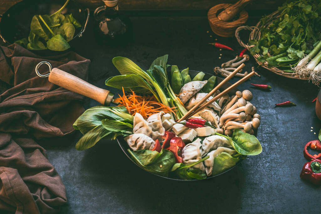Preparation of korean hot pot . Wok pan with vegetables and dumplings  on dark rustic kitchen table background with ingredients, top view. Copy space. - Foto, Bild
