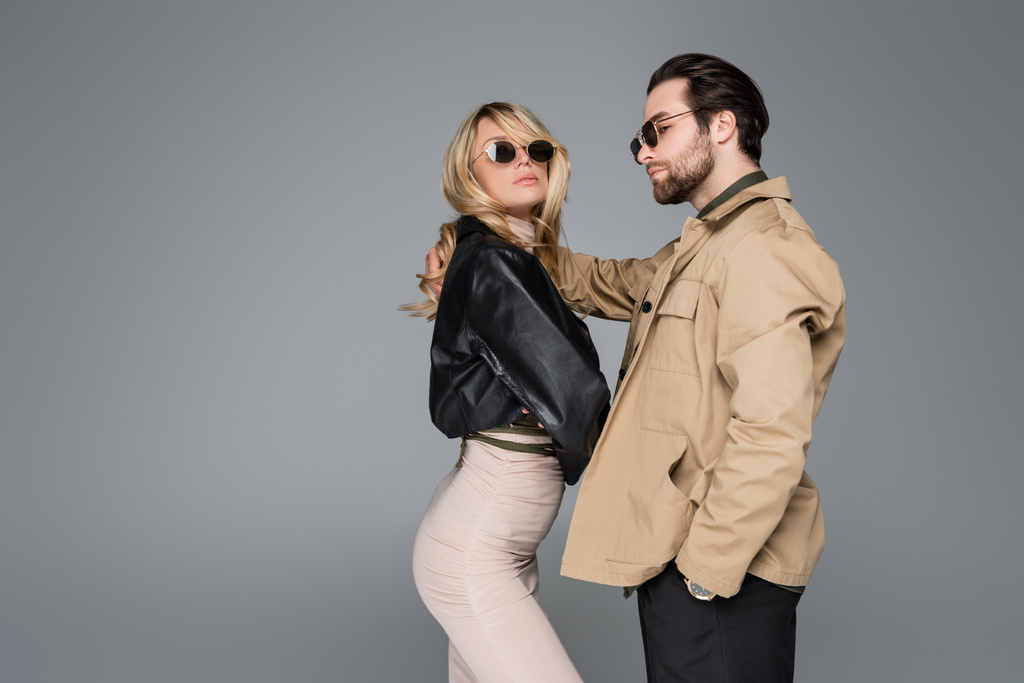 blonde woman in leather jacket and bearded man in sunglasses posing together isolated on grey - Photo, image