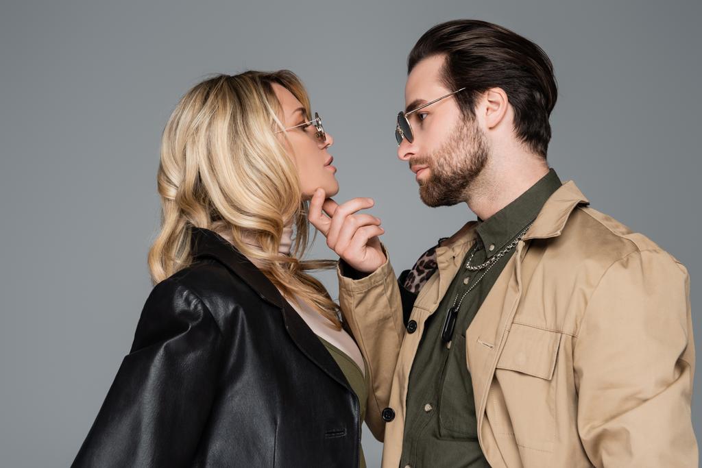 side view of bearded man in sunglasses touching face of blonde woman isolated on grey - Photo, Image