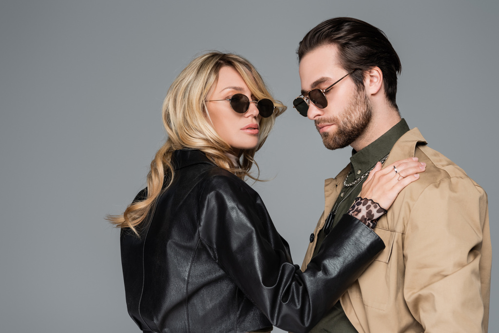 blonde in stylish black jacket woman hugging bearded man in sunglasses isolated on grey - Foto, immagini