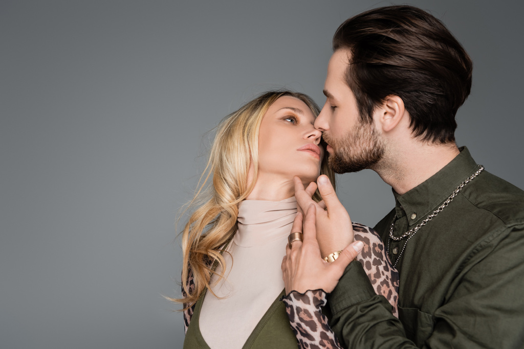 bearded man in green shirt kissing blonde girlfriend isolated on grey - 写真・画像