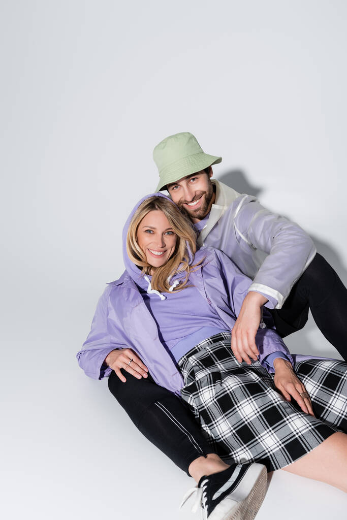 cheerful man in panama hat hugging blonde woman in tartan skirt while sitting on grey - Foto, imagen