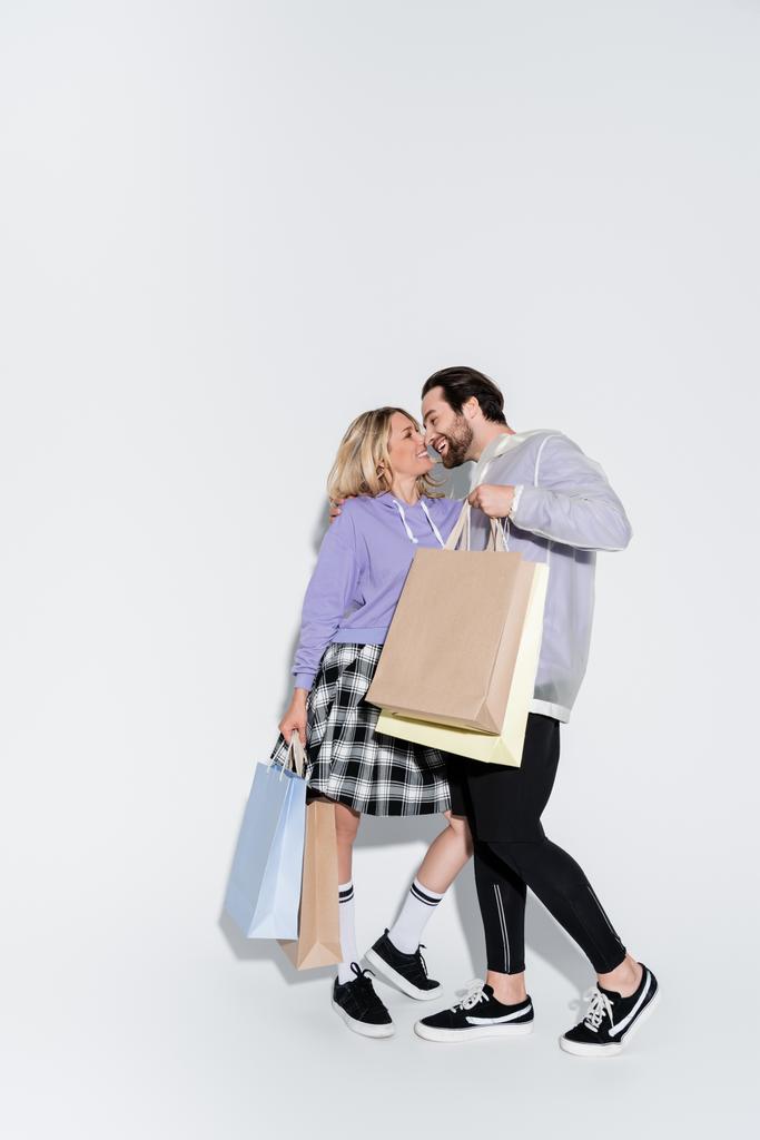 full length of happy man holding shopping bags near blonde woman in tartan skirt on grey - Foto, Imagem